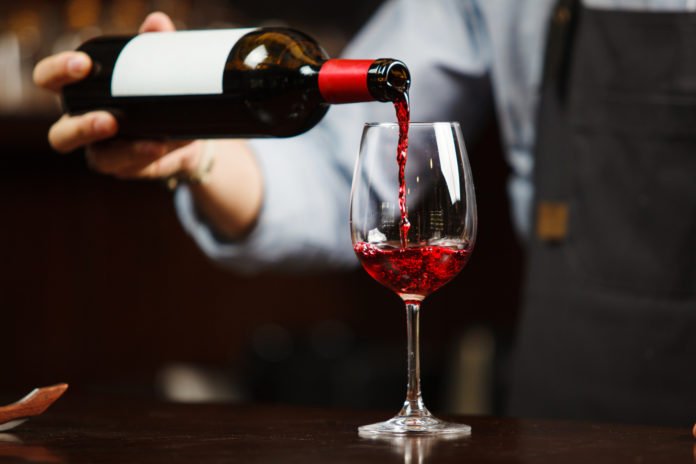 Waiter pouring red wine into wineglass. Sommelier pours alcoholic drink
