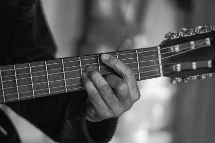 Mãos de um músico tocando violão acústico em uma fotografia em preto e branco.