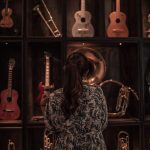 Visitante observa uma coleção de instrumentos musicais expostos em uma sala pouco iluminada.