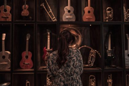 Visitante observa uma coleção de instrumentos musicais expostos em uma sala pouco iluminada.