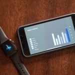 Smartphone e smartwatch exibem um relatório semanal de saúde sobre uma mesa de madeira.