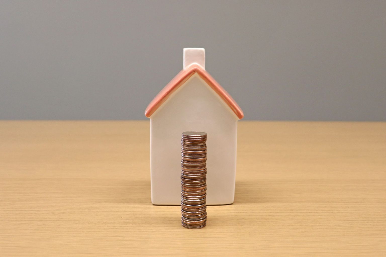 Moedas empilhadas diante de uma pequena casa de porcelana, representando economia e investimento imobiliário.