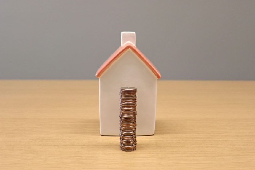 Moedas empilhadas diante de uma pequena casa de porcelana, representando economia e investimento imobiliário.