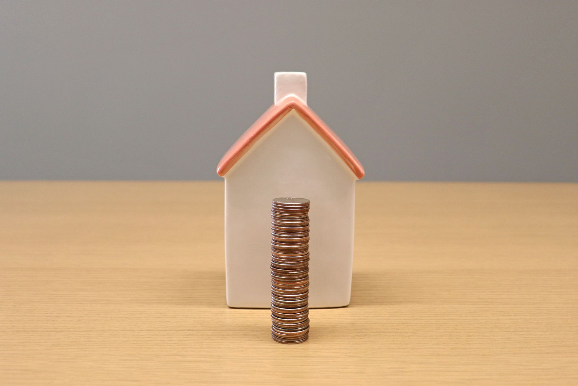 Moedas empilhadas diante de uma pequena casa de porcelana, representando economia e investimento imobiliário.