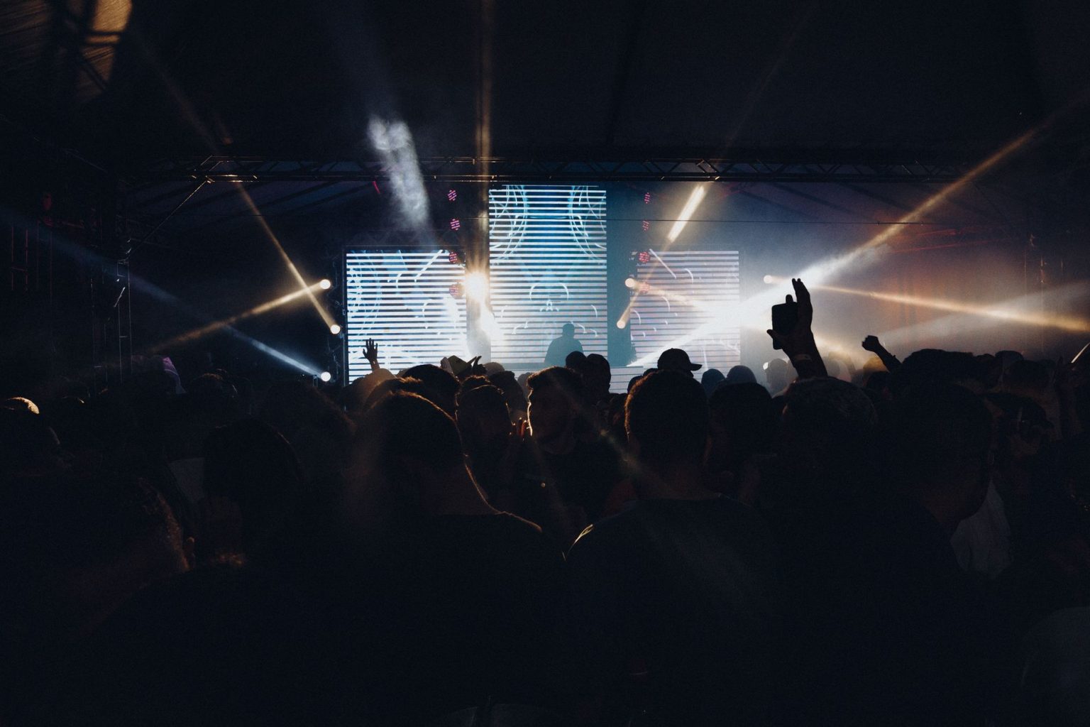 Público acompanha um show noturno ao ar livre, diante de um palco iluminado por luzes coloridas.