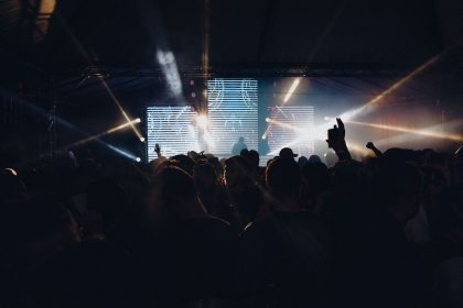 Público acompanha um show noturno ao ar livre, diante de um palco iluminado por luzes coloridas.